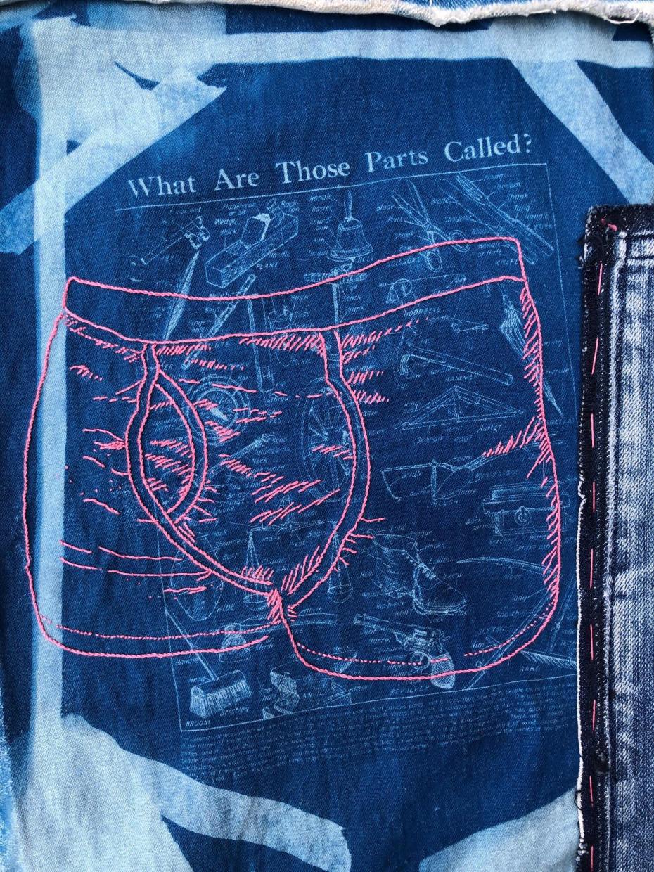 A photo of a piece of embroidery on printed denim. The print is in pale and deep blue, taken from a 1930s magazine illustration titled "what are those parts called?" with line drawings of labelled domestic tools and machinery. The embroidery stitched over the print is a pair of men's pants in thick pink thread.